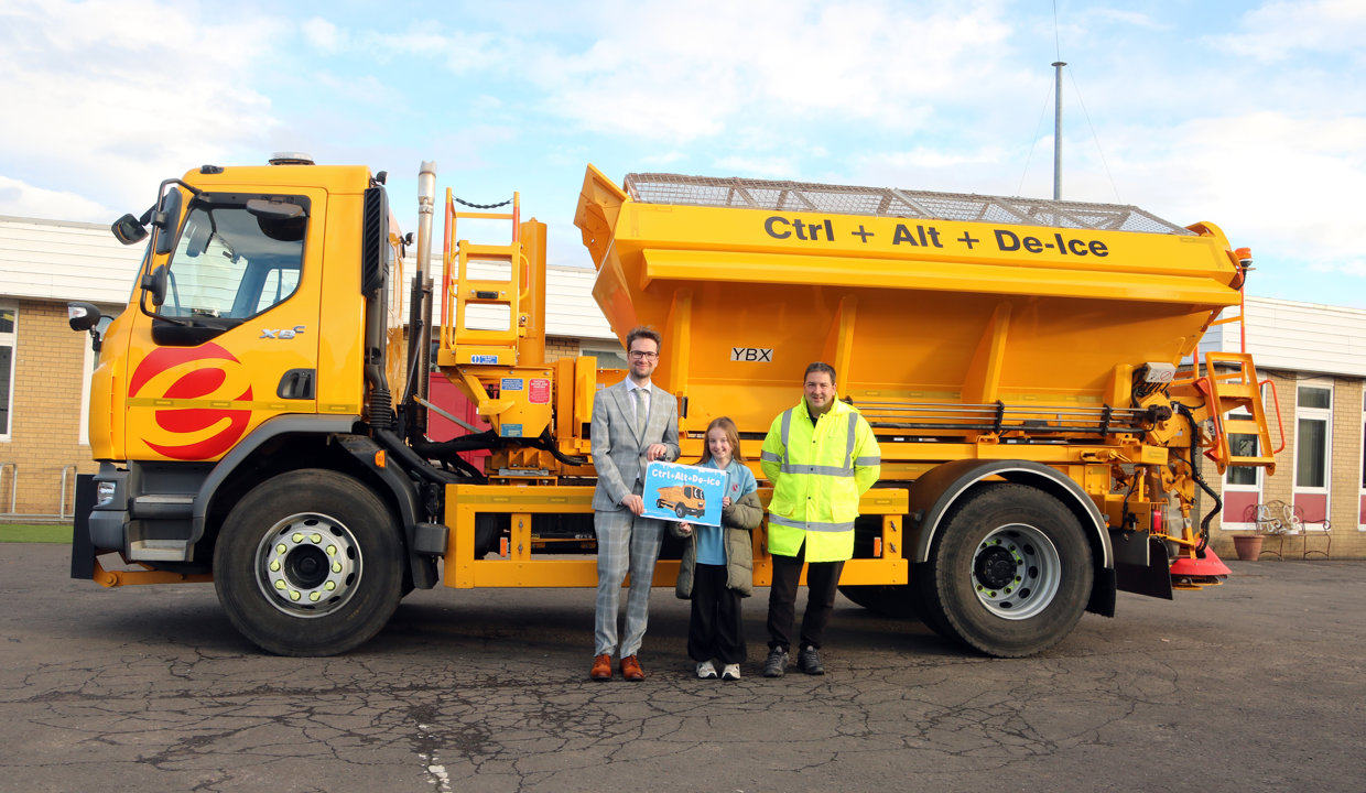 Councillor Paul Ferretti and Fleet manager present winning pupil with a certificate in front of a yellow gritting truck