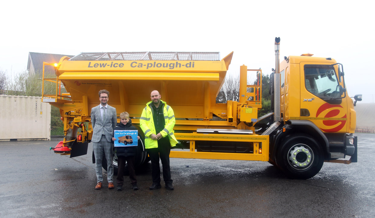 Councillor Paul Ferretti and Fleet manager present winning pupil with a certificate in front of a yellow gritting truck