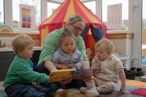 Childminder reading a book with three children
