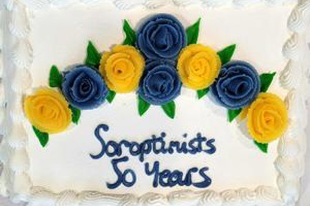 White iced cake, decorated with iced blue and yellow roses and the text ‘Soroptimists 50 Years’