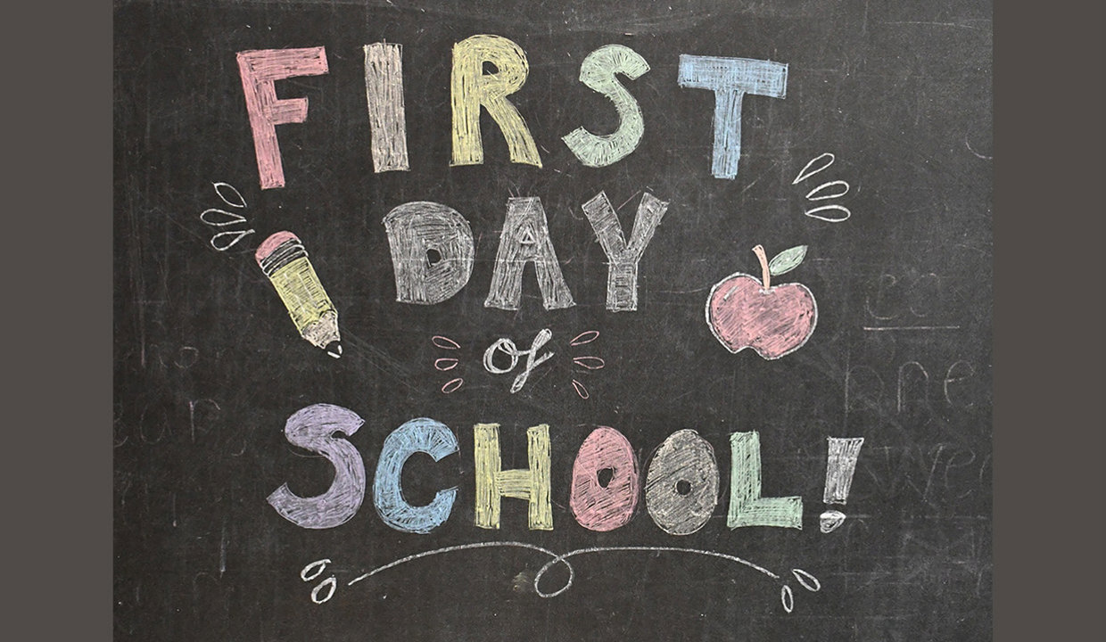A blackboard with the words First Day of School written in multicoloured chalk. 