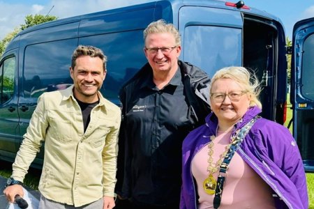Three people standing in front of blue van smiling.  Women to the right is wearing Provost’s chains
