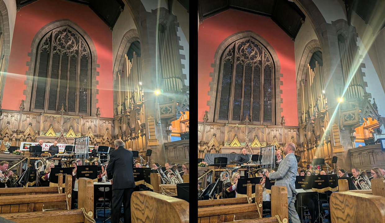 Inside of a church with large stained-glass window in background.  In the foreground is a band playing instrutments, led by a conductor with his back to the camera.  