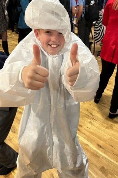 Boy wearing oversized forensic white suit holding his thumbs up to photographer