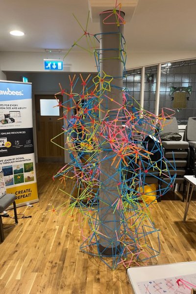 Brightly coloured plastic lengths replicating DNA structure, constructed around a large grey pillar 