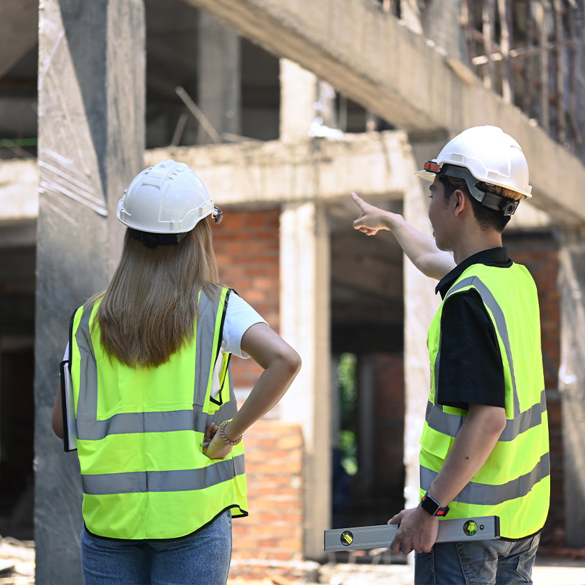 Two construction workers wearing helmets and high vis vests on a building site