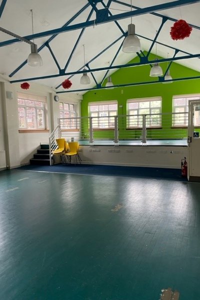mail hall with green and blue flooring and white walls and blue beams at ceiling height  and a small stage at the back